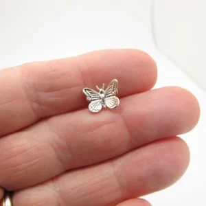 En närbild av en hand som håller Örhänge med stift - Fjäril, ett litet fjärilsformat örhänge i silver, mot en vit bakgrund.