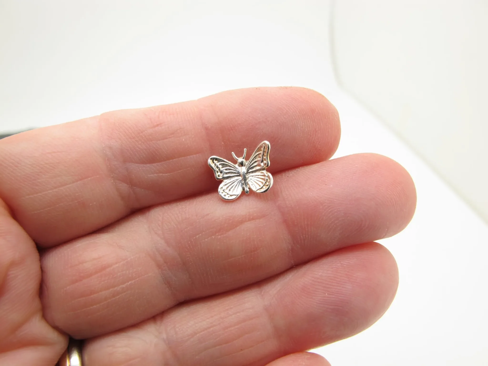 En närbild av en hand som håller Örhänge med stift - Fjäril, ett litet fjärilsformat örhänge i silver, mot en vit bakgrund.