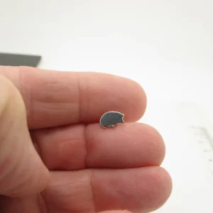 En person håller en Örhänge med stift - Igelkott, ett litet igelkottsformat örhänge i silver, på sina fingertoppar mot en vit bakgrund.