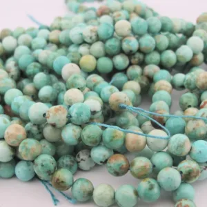 Närbild av flera strängar Krysokoll grön-blå ädelsten 6mm runda pärlor, i grönblå nyanser med brun och vit marmorering, löst lindade och trädda på blått snöre.