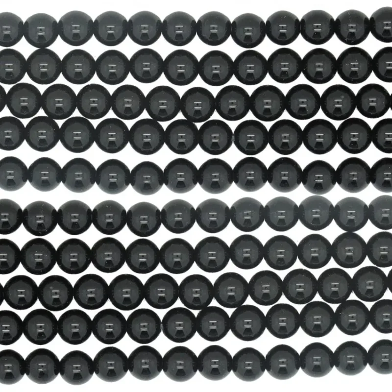 Rader av blanka, runda Svart rund onyx eller agat-pärlor (4-10 mm) är tätt placerade i ett snyggt, horisontellt mönster mot en vit bakgrund.