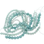 En härva av Amazonit rund ädelsten 6mm ljusblå och turkosa runda pärlor på blåa snören, arrangerade i lösa öglor mot en vit bakgrund.