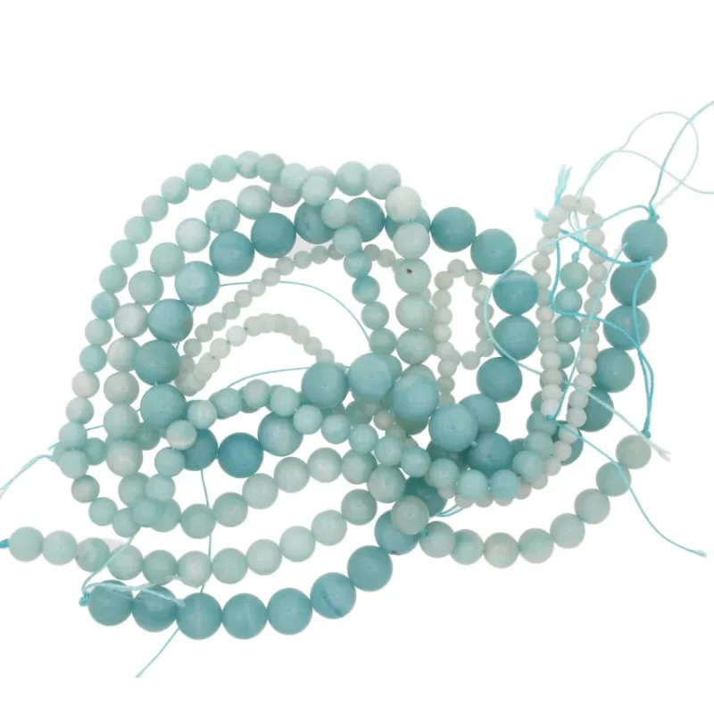 En härva av Amazonit rund ädelsten 6mm ljusblå och turkosa runda pärlor på blåa snören, arrangerade i lösa öglor mot en vit bakgrund.