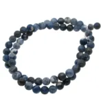 En löst slingrad tråd av Sodalit rund ädelsten 4-6 mm pärlor, med runda polerade blå och mörkblå ädelstenar, visas mot en vit bakgrund.