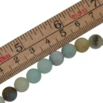 En rad Amazonit flerfärgad rund smyckesten 6mm pärlor är uppradade under en trälinjal märkt i tum och centimeter.