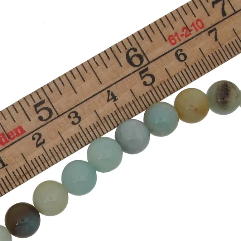En rad Amazonit flerfärgad rund smyckesten 6mm pärlor är uppradade under en trälinjal märkt i tum och centimeter.