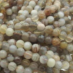Närbild på Karneol rund ädelsten enfärg 4-6 mm pärlor i polerade neutrala toner - brunt, grått, grädde och beige - varav vissa har band- eller randmönster.