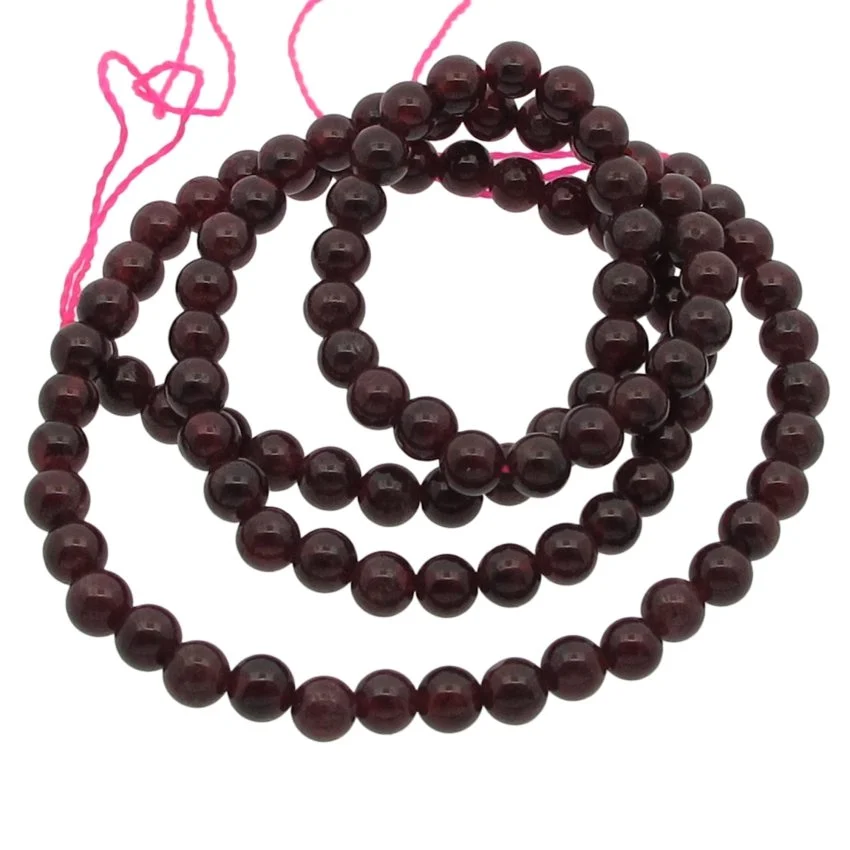 Granat 4mm rund ädelsten 1 En tråd av Granat rund ädelsten 4mm, med runda mörkröda pärlor, är upprullad mot en vit bakgrund med ett rosa snöre synligt i ena änden.