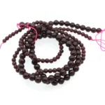 En spiralformad tråd av 4 mm Granat rund ädelstenspärlor, djupröda och runda, trädda med ljusrosa snöre och mot en vit bakgrund.