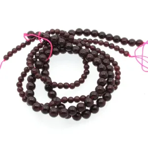 En spiralformad tråd av 4 mm Granat rund ädelstenspärlor, djupröda och runda, trädda med ljusrosa snöre och mot en vit bakgrund.