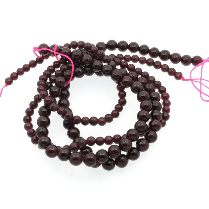 En spiralformad tråd av 4 mm Granat rund ädelstenspärlor, djupröda och runda, trädda med ljusrosa snöre och mot en vit bakgrund.