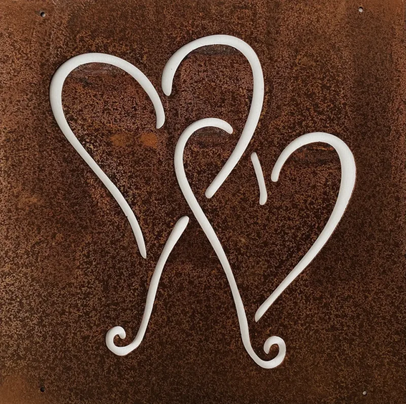 The Hund dekorplåt för armeringsnät 14x14cm är en rostfärgad metallpanel med tre stiliserade hjärtformade utskärningar som släpper igenom ljus och framhäver kontrasten mellan panelen och dess bakgrund.