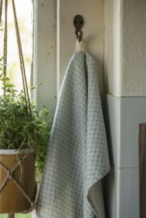 En ljusblå mönstrad handduk hänger på en Krok enkel mini 3x6cm väggkrok nära ett fönster, med en krukväxt i en makraméhängare synlig till vänster.