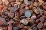 En hög med Karneol rund ädelsten enfärg 4-6 mm stenar i nyanser av rött, brunt och orange, med ett kinesiskt 1 yuan-mynt bland dem för storleksjämförelse.