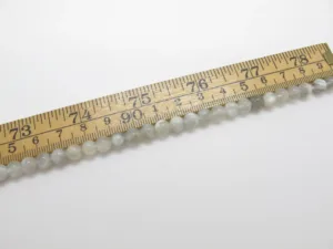 En Månsten rund ädelsten 6mm pärlsträng - en rad med små, runda, ljusa pärlor - mäts med en trälinjal som är märkt i tum och centimeter.
