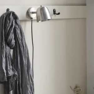 En ljusgrå scarf hänger från en Krok dubbel mini - mässing krok på en benvit väggmonterad hylla. I närheten hänger en silverfärgad vägglampa med svart sladd och en annan tom mässingskrok är synlig. Bakgrundsväggen är offwhite.