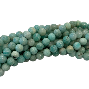 Blue-green, round gemstone beads piled in a corner on a white background, glossy and marbled in color.