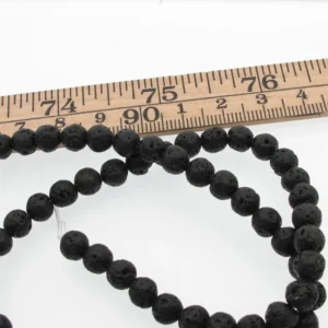 En sträng med Lavasten svarta runda 4-8 mm vaxade pärlor, svarta, runda och porösa, är upprullad bredvid en linjal märkt i tum; pärlorna mäter ca 8 mm i diameter.