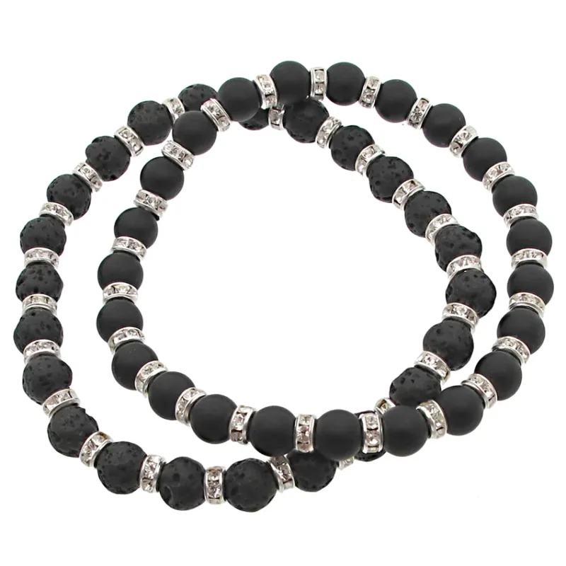 Lavasten svarta runda 4-8mm vaxade halsband har omväxlande matta och texturerade svarta lavapärlor, åtskilda av silverfärgade distansringar med små klara kristaller. Halsbandet visas här upprullat i en lös spiral.