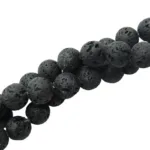 Närbild på Lavasten svarta runda 4-8 mm vaxade pärlor med runda, svarta, vaxade lavastenar med porös textur, diagonalt placerade mot en vit bakgrund.