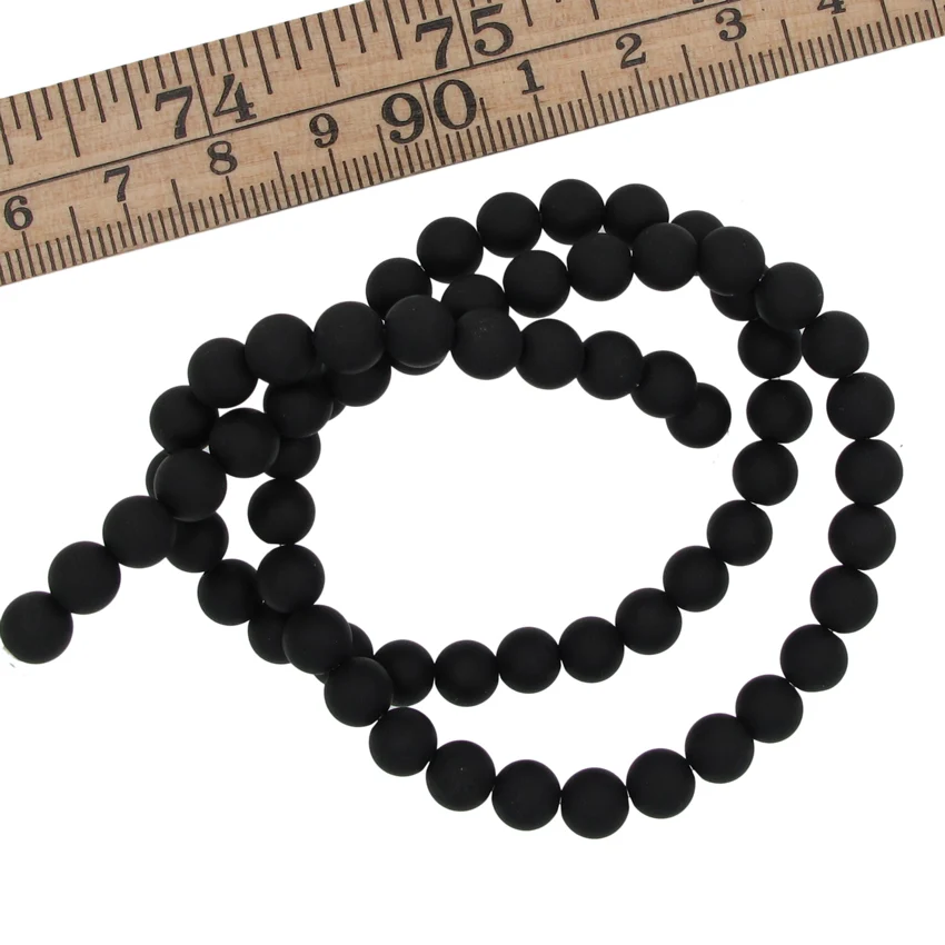 Svart Agat 6mm rund ädelsten 3 Ett pärlband med Karneol rund ädelsten enfärg 4-6 mm pärlor är arrangerat i en lös spiral under en trälinjal, vilket visar att de runda ädelstenspärlorna är ca 4-6 mm i diameter.