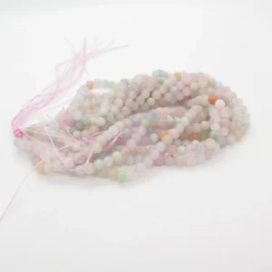 En bunt Karneol rund ädelsten enfärg 4-6mm pastellfärgade runda pärlor, huvudsakligen rosa, gröna och blå, trädda med lösa rosa snören på en vit yta.
