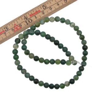 Mossagat-rund6_2 - Fredrix Design & Smyckerian En slinga med Mossagat rund ädelstenspärlor, var och en cirka 8 mm i diameter, placeras bredvid en trälinjal markerad i centimeter.