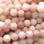 Närbild på Karneol rund ädelsten enfärg 4-6 mm pärlor med blank, polerad yta, uppträdda i flera trådar. De släta, runda pärlorna finns i mjuka nyanser av rosa, grädde och persika.