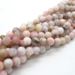 Närbild av Karneol rund ädelsten enfärg 4-6mm pärlor i mjuka rosa, vita, beige och ljusbruna toner med naturlig marmorering och inneslutningar, trädda tillsammans på rosa tråd.