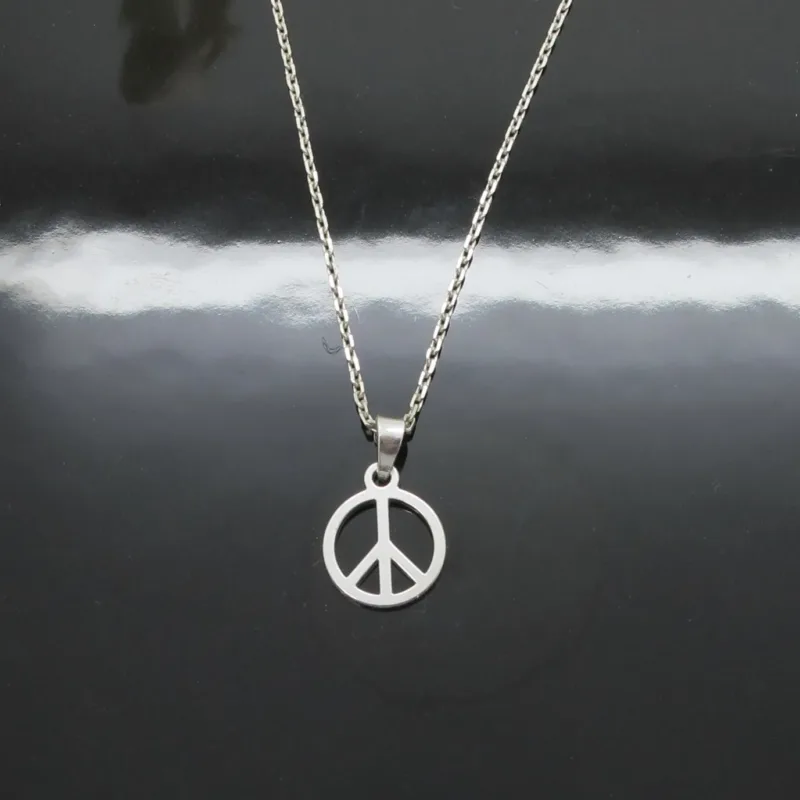 Ett silverhalsband med ett hänge med en fredssymbol som visas på en blank svart yta med en tydlig reflektion av kedjan och berlocken.