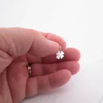 En hand som håller i en liten silverfärgad fyrklöverberlock mot en vit bakgrund.