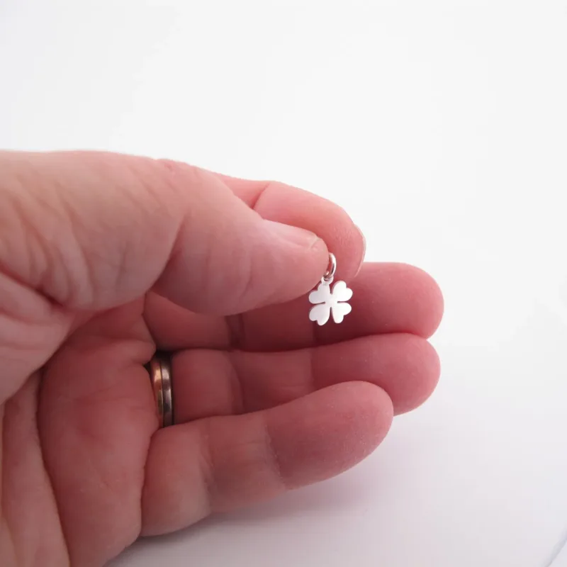 En hand som håller i en liten silverfärgad fyrklöverberlock mot en vit bakgrund.