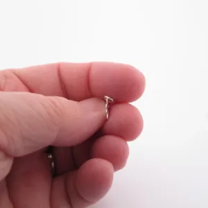 Närbild av en hand som håller i ett litet silverörhänge mot en vit bakgrund.