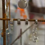 Tre hamrade silverringar hänger från en rostig metallstång, med andra smycken och suddiga föremål synliga i bakgrunden.