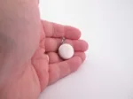 Närbild av en hand som håller i en rund silvermedaljong mot en vit bakgrund.