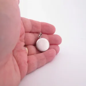 Närbild av en hand som håller i en rund silvermedaljong mot en vit bakgrund.