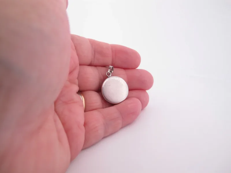 Närbild av en hand som håller i en rund silvermedaljong mot en vit bakgrund.