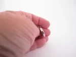 En hand håller i ett litet ringformat silverhänge mot en vit bakgrund.