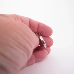 En hand håller i ett litet ringformat silverhänge mot en vit bakgrund.