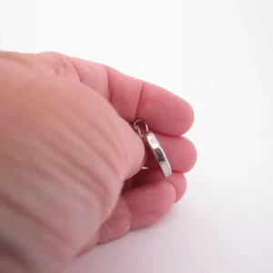 En hand håller i ett litet ringformat silverhänge mot en vit bakgrund.