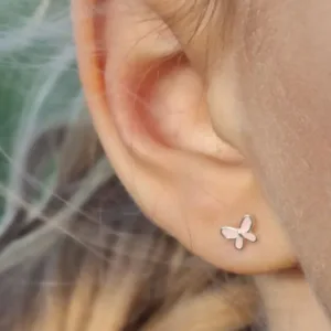 Närbild av en persons öra som bär ett litet fjärilsformat örhänge i silver. Bakgrunden är mjukt suddig, vilket framhäver örhänget och en del av personens hår.