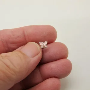 Närbild av en hand som håller i ett litet fjärilsformat örhänge i silver mot en vit bakgrund.