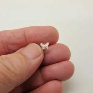 Närbild av en hand som håller i ett litet fjärilsformat örhänge i silver mot en vit bakgrund.