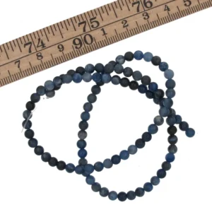 En tråd med runda, mörkblå Sodalit rund ädelstenpärlor (4-6 mm) är upprullad bredvid en trälinjal märkt i tum och centimeter.