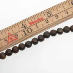 En trälinjal märkt i centimeter och märkt Sverige mäter Bronsit rund ädelsten 6mm pärlor, varje pärla cirka 6 millimeter i diameter.