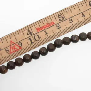 En trälinjal märkt i centimeter och märkt Sverige mäter Bronsit rund ädelsten 6mm pärlor, varje pärla cirka 6 millimeter i diameter.