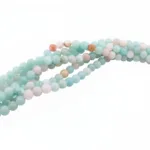 Flerfärgade runda smyckestenar av amazonit, 6mm, i ljusblått med inslag av vitt, persika och beige, arrangerade i ett löst, tvinnat mönster mot vit bakgrund.