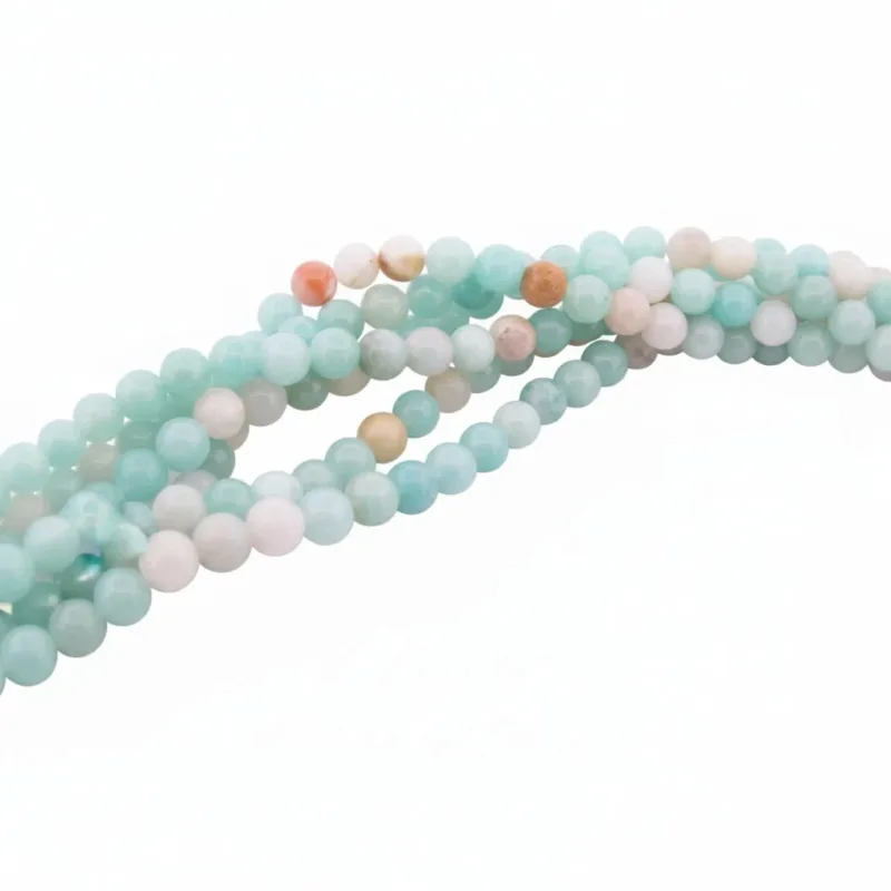 Flerfärgade runda smyckestenar av amazonit, 6mm, i ljusblått med inslag av vitt, persika och beige, arrangerade i ett löst, tvinnat mönster mot vit bakgrund.