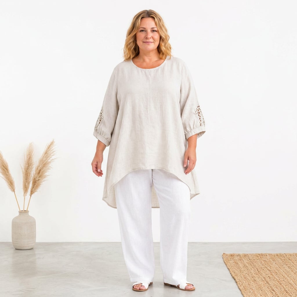 Woman wearing a loose beige linen tunic with crochet-sleeve details and white wide-leg pants in a bright studio setting.