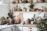 En mysig kökshörna dekorerad inför julen med Pepparkakshus för ljus med snökristall, trähyllor med tallrikar, muggar, burkar, vintergröna grenar, jultomtar och ett tänt ljus för en festlig stämning.